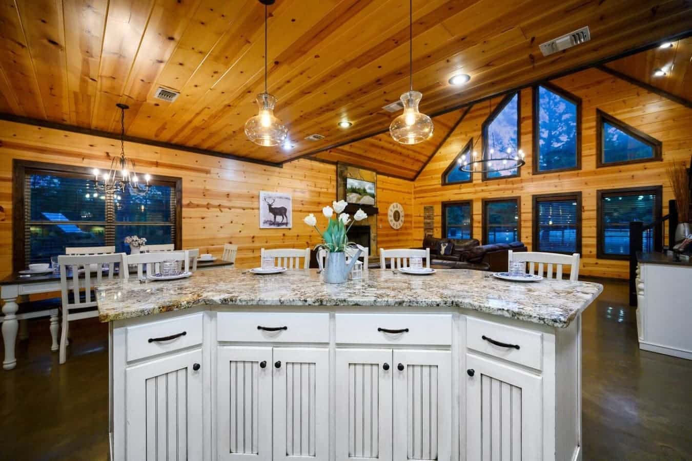 With those pendant lights hanging over the granite island, white farmhouse cabinetry, and windows framing the twilight forest all around, this kitchen feels like the place where everyone naturally ends up gathering.