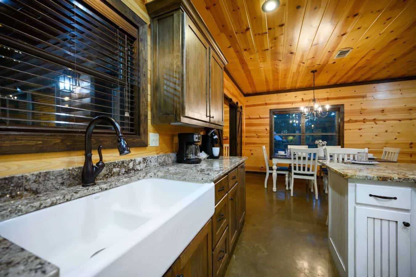 The wood-lined kitchen flows straight into the dining area with those big windows framing the twilight forest, making it feel like cooking and eating are just an excuse to stay connected to the view outside.