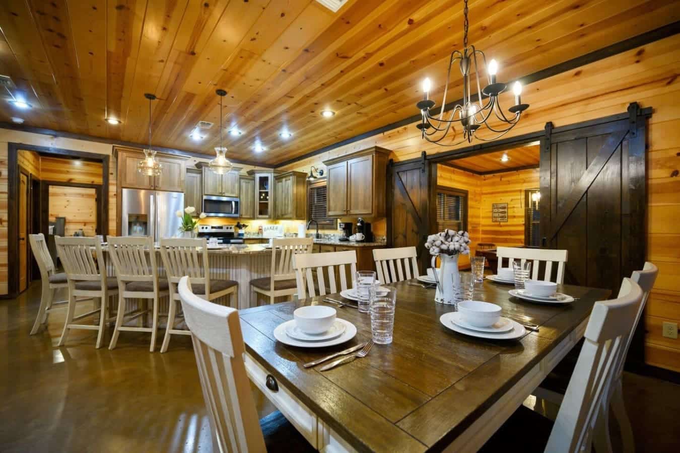 This dining room setup with those cream and wood chairs, the dark stained table, and the barn doors opening to the rest of the cabin basically invites everyone to sit down together and actually spend time with each other.