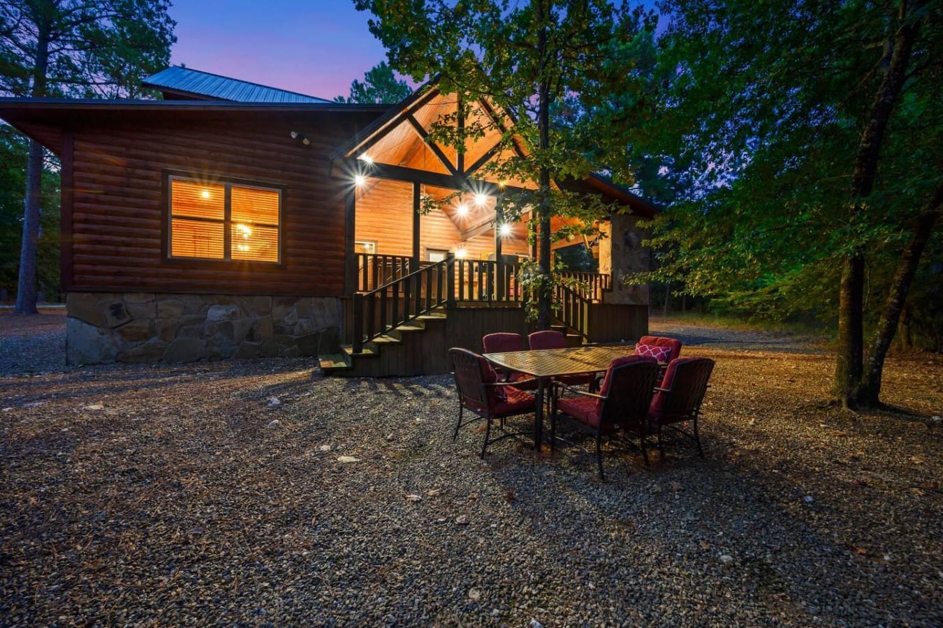 Evening settles in and the cabin glows warm against the darkening trees, with that inviting patio setup calling you to pull up a chair and stay awhile.