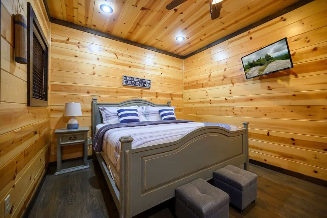 This bedroom wraps you in warm pine walls and natural wood beams, with a sturdy four-poster bed and those blue-striped pillows that practically scream "time to actually rest and unwind."