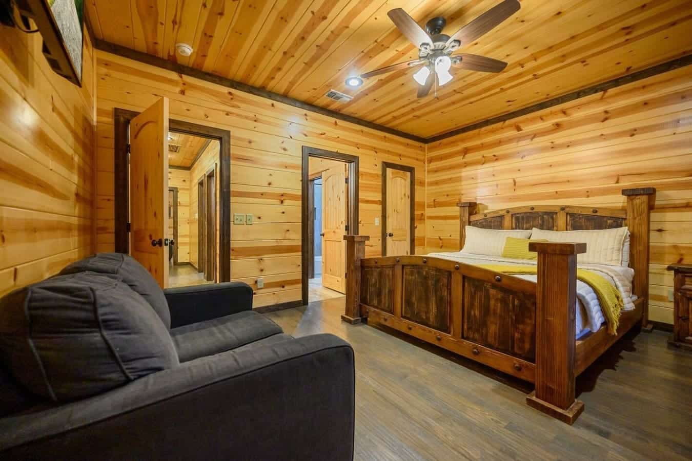 This master bedroom wraps you in warm wood from floor to ceiling, complete with a rustic bed, a cozy seating nook, and multiple doors opening to different parts of the cabin—basically your own private retreat within the retreat.