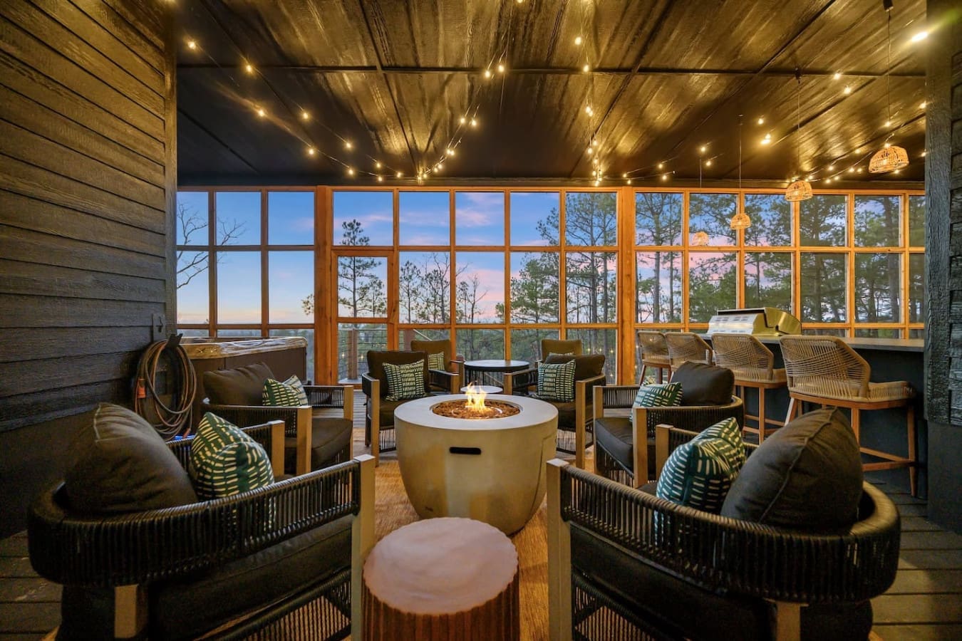 Picture yourself cozied up in one of those comfy woven chairs around a crackling fire pit, surrounded by floor-to-ceiling windows framing the forest and sky as the sun dips below the treeline.