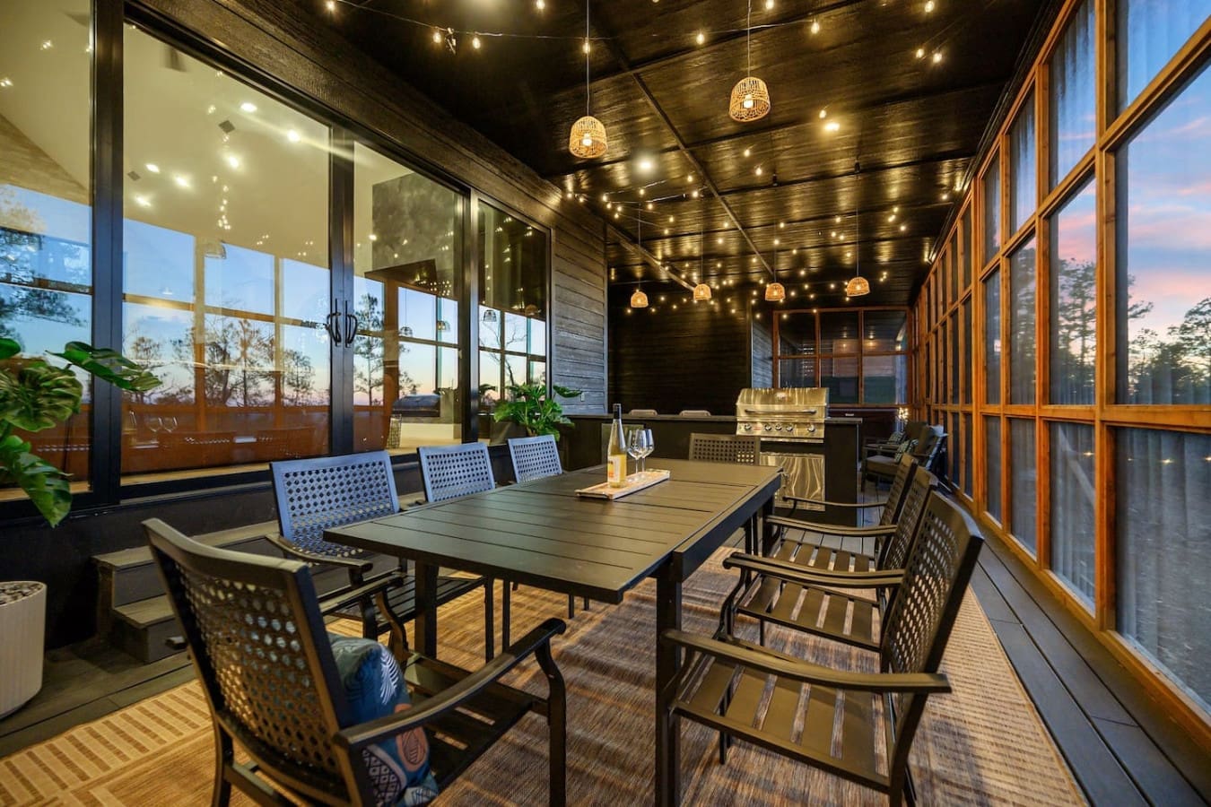 This covered outdoor dining space is absolutely perfect for gathering everyone together as the sun sets, with those golden string lights twinkling overhead and views stretching out through the windows on both sides.