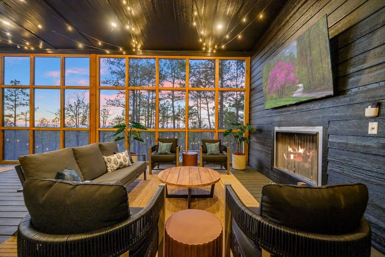This cozy fireside lounge has everything you'd want for a perfect evening—plush seating, a real fireplace, those massive windows framing the twilight forest, and string lights twinkling overhead.