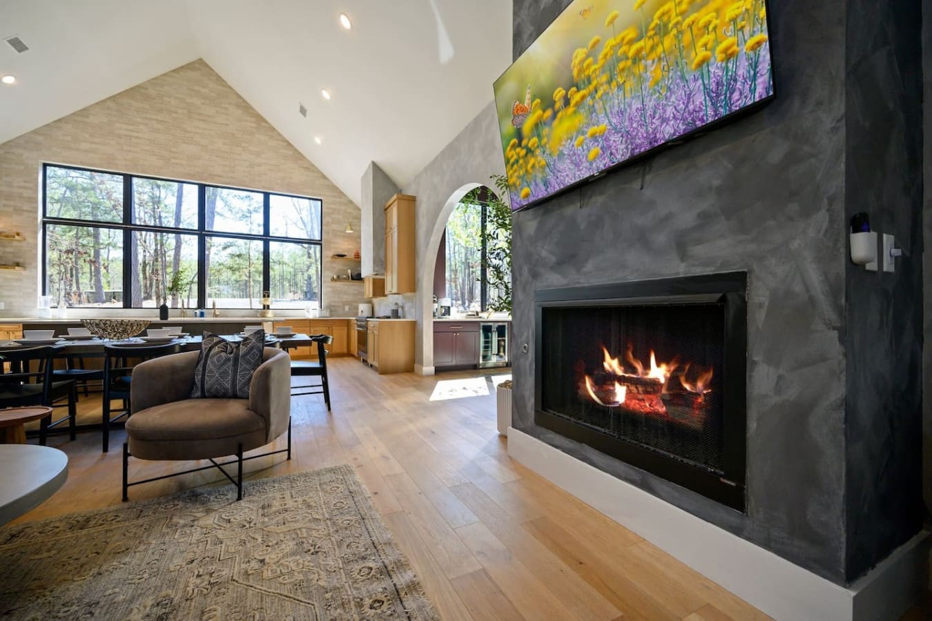 This soaring open-concept space with its dramatic fireplace, cozy seating nook, vibrant wildflower art, and those floor-to-ceiling windows is basically the perfect spot to settle in for the evening—whether you're watching the flames flicker or catching th