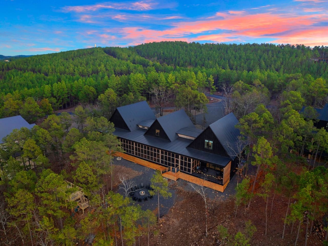 This modern architectural gem tucked into the pines with its dramatic black rooflines and expansive wood deck is basically the ultimate forest escape—like something straight out of a design magazine, but actually cozy enough to call home.