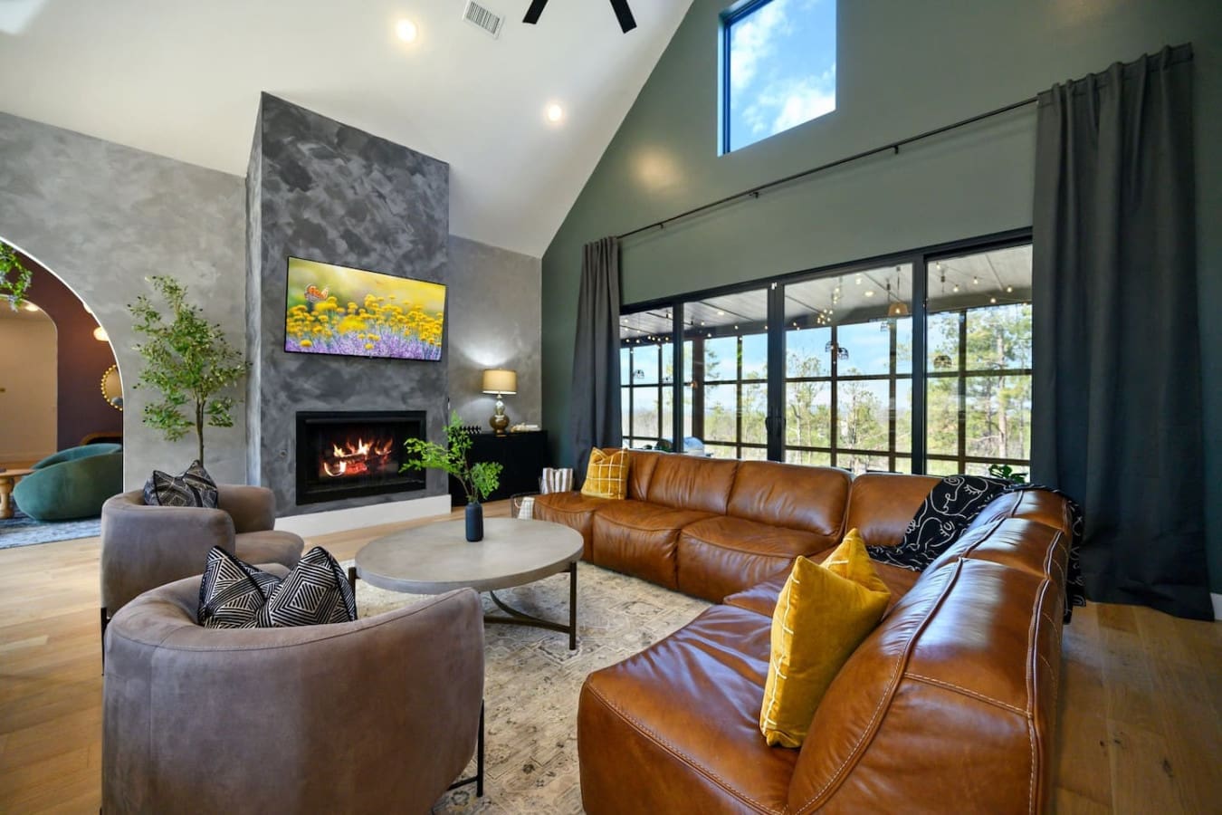 This open-concept living room is basically built for lounging—you've got that gorgeous fireplace anchoring the space, leather seating that invites you to sink in, those floor-to-ceiling windows flooding everything with natural light, and views of the fore