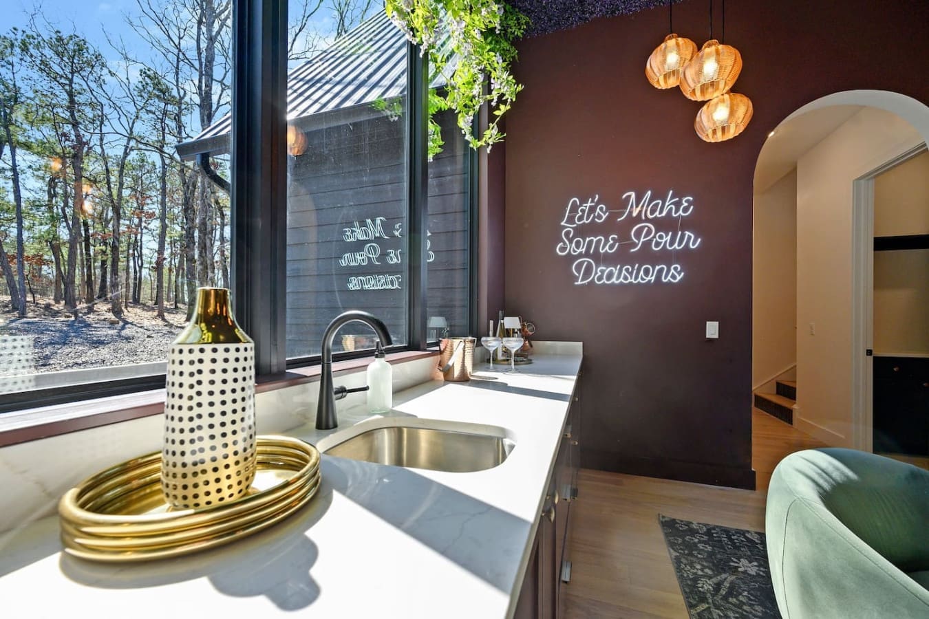 This wine bar setup with those amber pendant lights and cheeky neon sign is basically calling your name for an evening of good conversations and forest views through those massive windows.