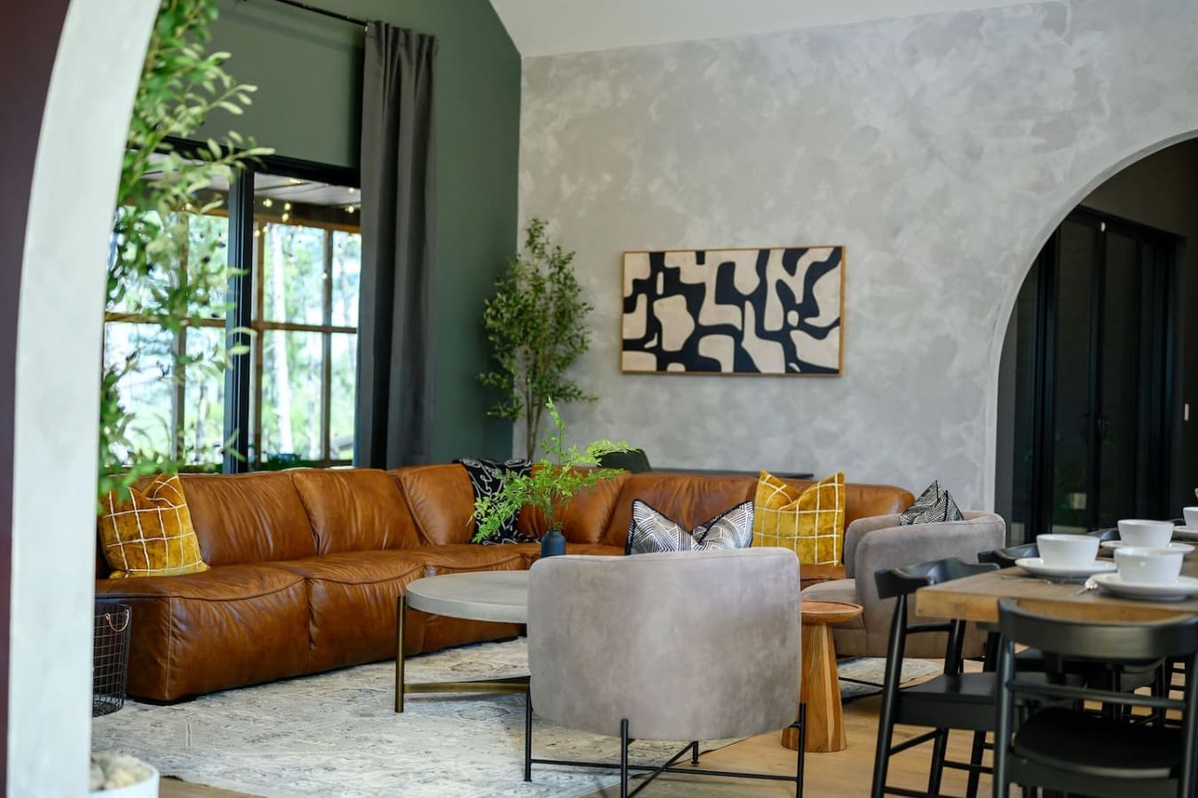 This living room is basically the perfect blend of cozy and cool with that cognac leather sectional, those pops of mustard yellow, and enough plants scattered around to make you forget you're technically still indoors.