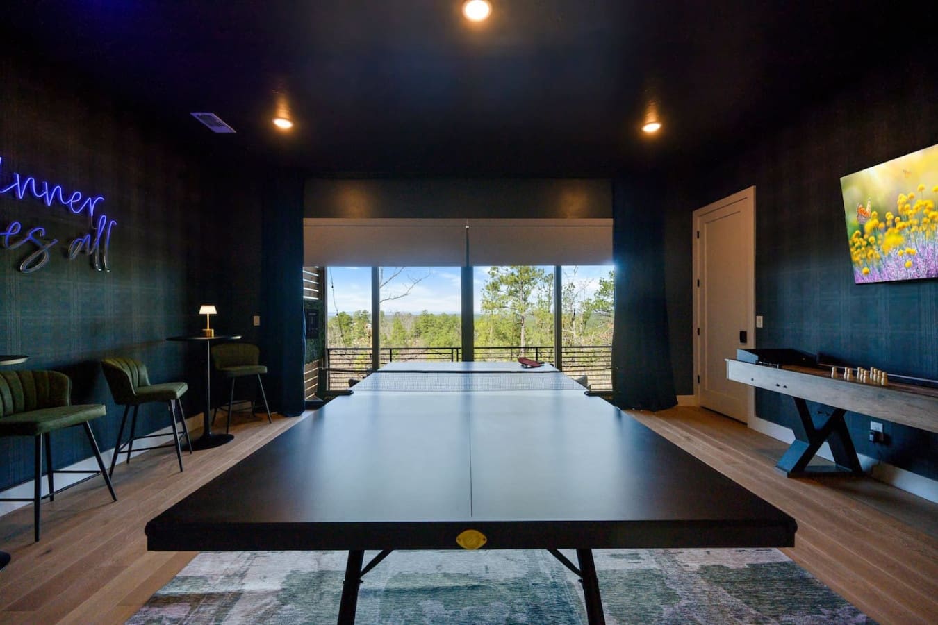 This sleek game room with its ping pong table front and center, air hockey setup off to the side, and those floor-to-ceiling windows framing the forest is basically built for friendly competition and good times with a view.