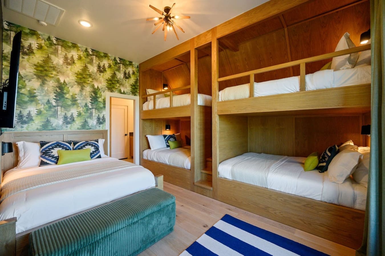 This spacious bunk room with its built-in wood sleeping nooks and forest-themed wallpaper is basically a kid's dream—plenty of cozy spots for the whole crew with that natural wood warmth and playful vibe throughout.