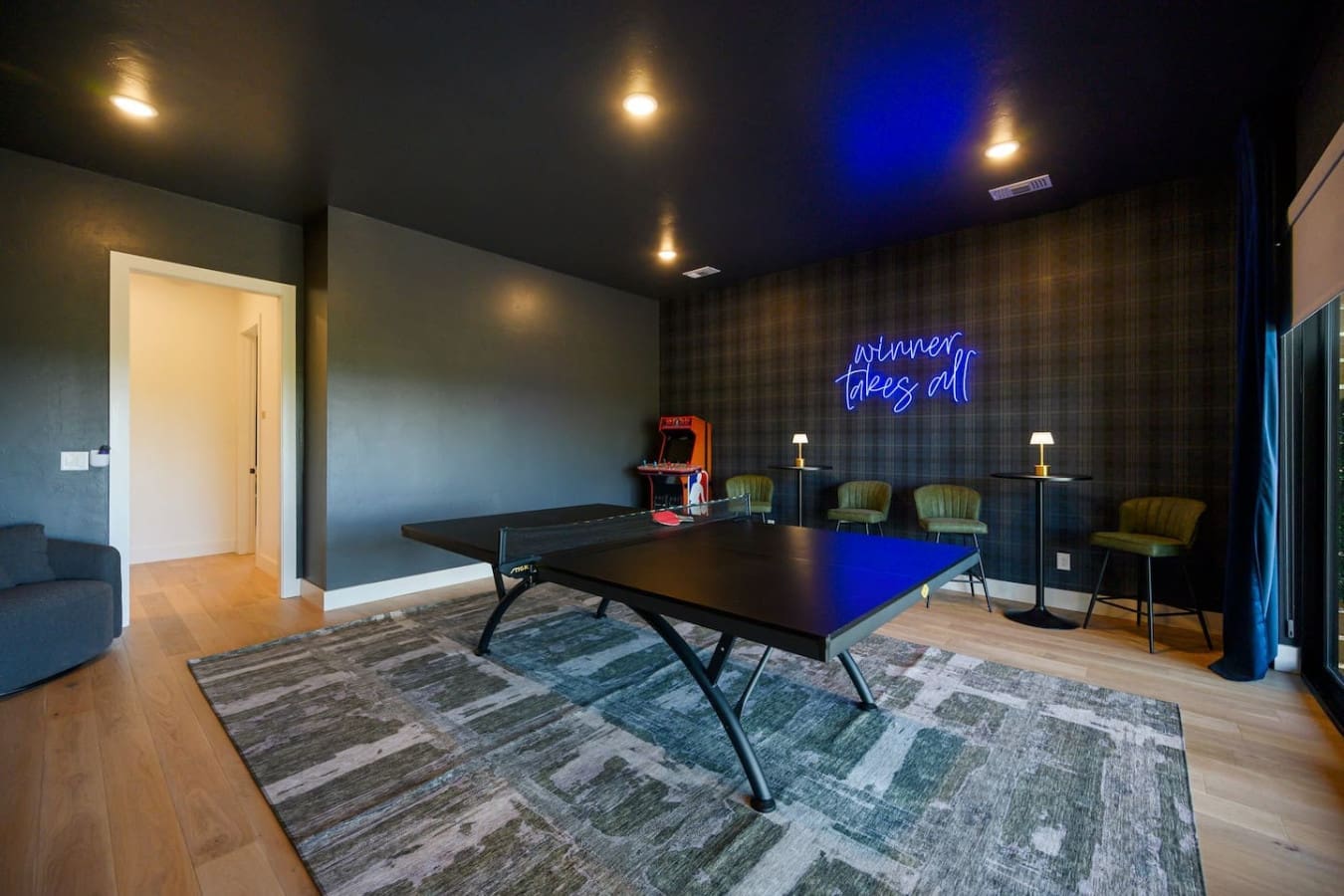 This game room is basically the ultimate hangout spot—ping pong table, vintage arcade machine, those cozy sage chairs, and that cheeky neon sign all set against moody walls and dramatic lighting that just screams "let's have some fun tonight."