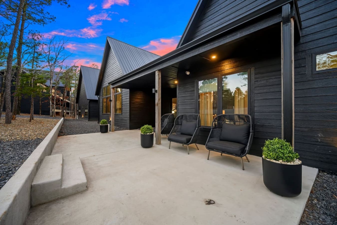 This modern patio is basically your front-row seat to the sunset with those sleek black chairs perfectly positioned to take in the twilight sky, while the warm glow from inside the home creates that cozy transition from day to night.