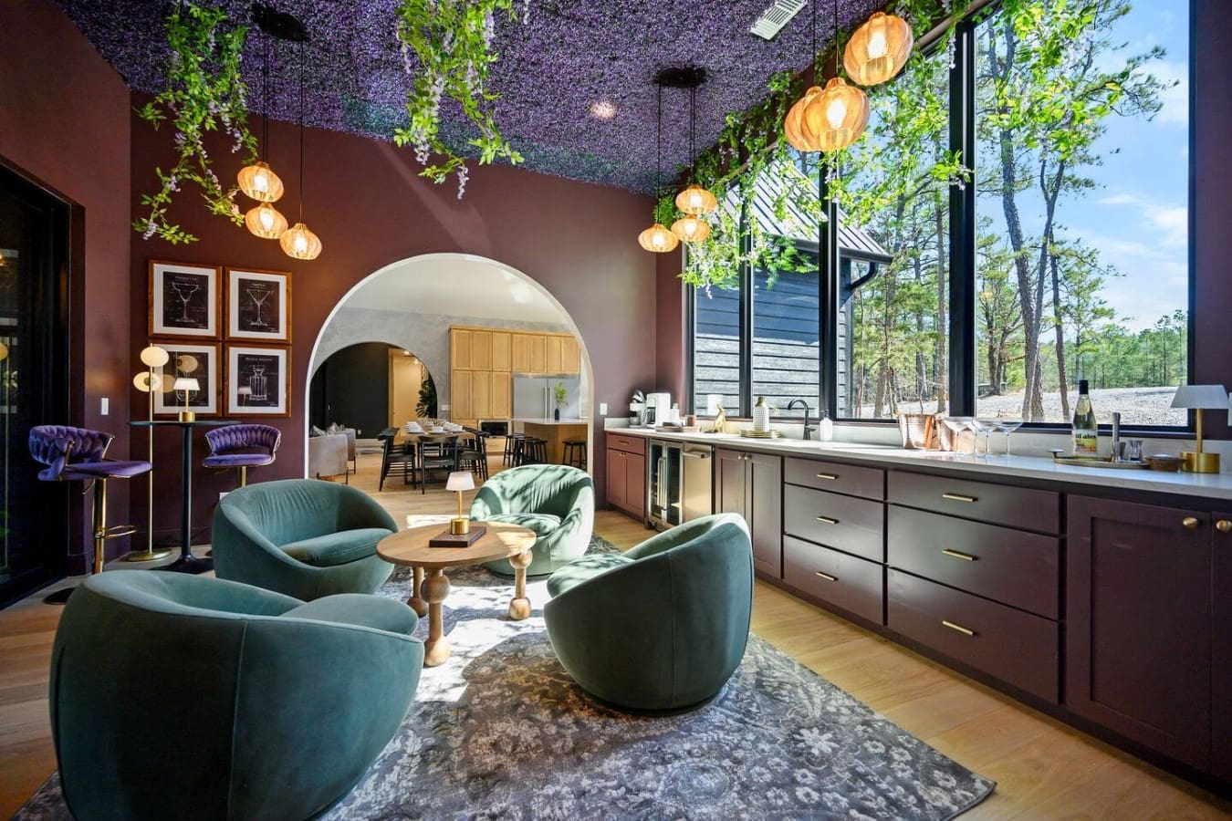 This open-concept living space with its moody burgundy walls and lush hanging greenery feels like the perfect spot to settle in with those cushy teal chairs and soak in the forest views.
