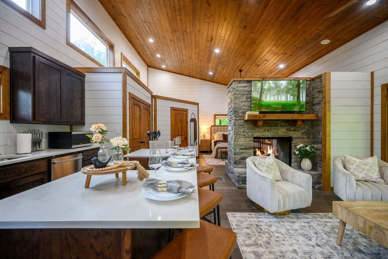 The vaulted wood ceiling, warm stone fireplace, and flowing open layout make this the kind of space where everyone naturally gravitates and somehow ends up staying way longer than planned.