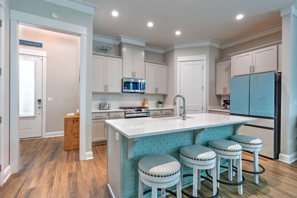 This kitchen island is basically the heart of the whole place—three stools pulled up to a pristine white countertop, turquoise subway tile backing, and enough room to hang out while someone's actually cooking something good.