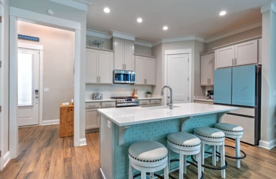 This kitchen island is basically the heart of the whole place—three stools pulled up to a pristine white countertop, turquoise subway tile backing, and enough room to hang out while someone's actually cooking something good.