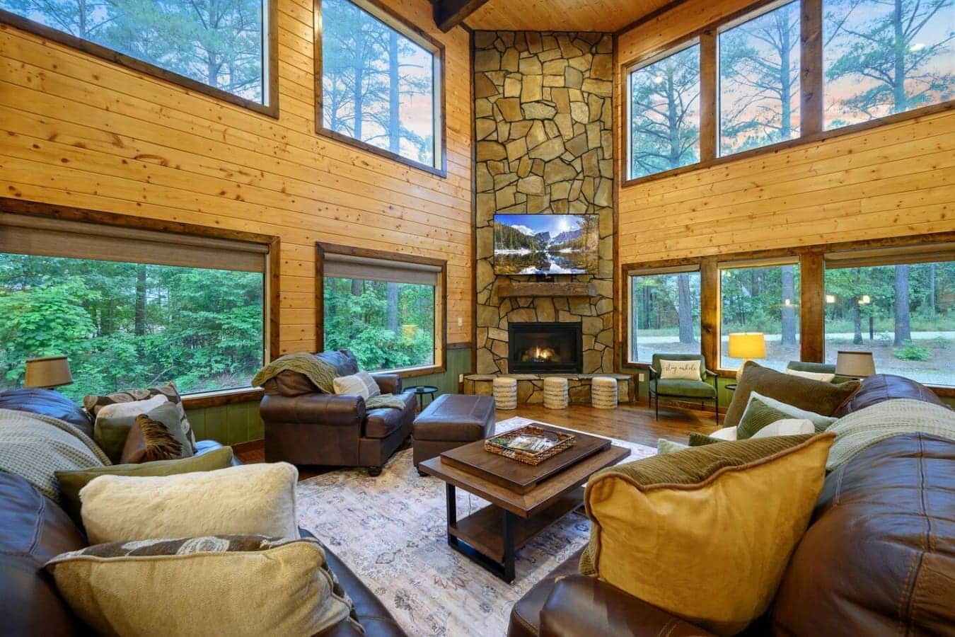 This living room just gets it—high ceilings, a stone fireplace, windows everywhere so you're basically living in the trees, and enough seating that your whole group can actually hang out together without fighting over spots.