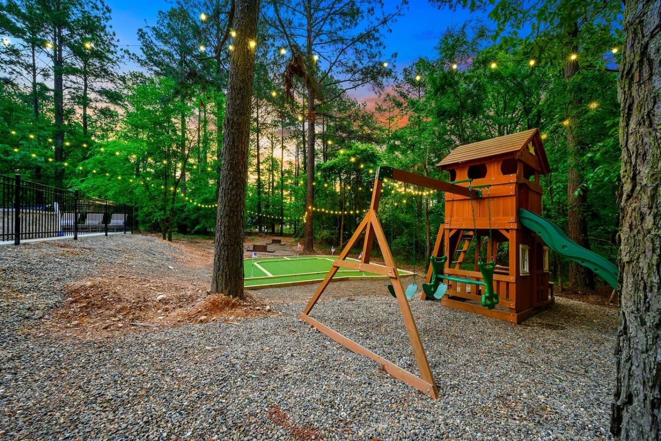 Your kids (and let's be honest, the adults too) are gonna lose their minds over this wooden playset tucked into the trees with string lights overhead.