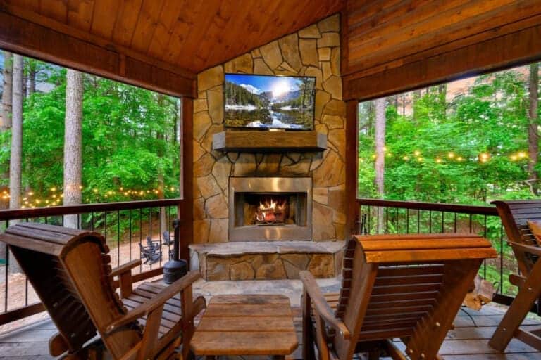 This screened porch setup is legit the sweet spot—fireplace going, TV mounted above, wood everywhere, and those forest views on all sides so you can actually relax without feeling cooped up.