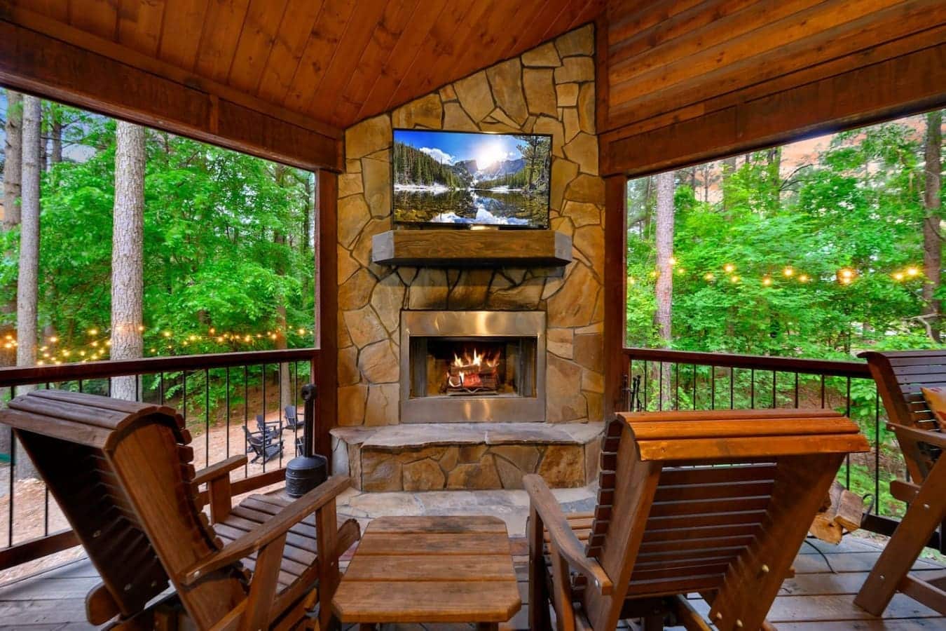 This screened porch setup is legit the sweet spot—fireplace going, TV mounted above, wood everywhere, and those forest views on all sides so you can actually relax without feeling cooped up.