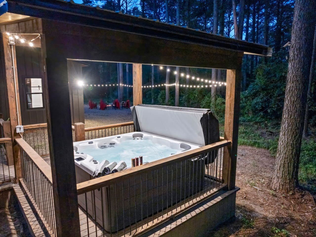 Unwind in the private hot tub under twinkling string lights, surrounded by peaceful woods and cozy vibes.