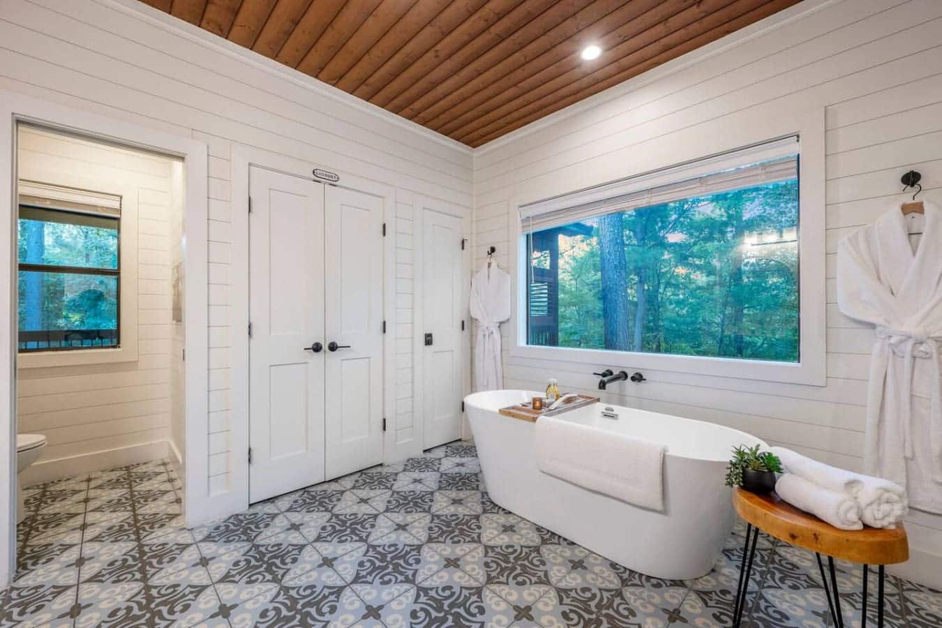 This primary bathroom is basically a spa retreat situation with that soaking tub positioned perfectly to stare out at the trees, double vanity so nobody's fighting for space, and those huge windows that make you feel like you're bathing in the forest.