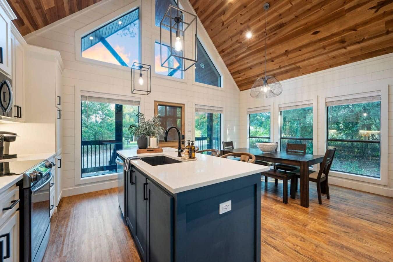 This kitchen and dining setup basically has you covered for everything—cook at that gorgeous island, eat at the table, and hang in the living area all while those floor-to-ceiling windows keep the forest views front and center.