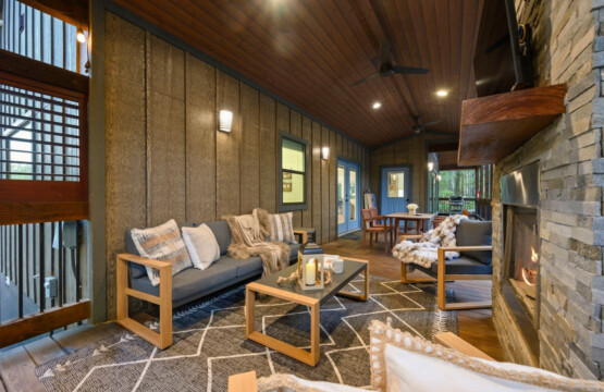 This living room is basically designed for those moments where you just want to sink into the sofa with a blanket, stare out at the trees through those huge windows, and let the wood walls and fireplace remind you why you came here in the first place.