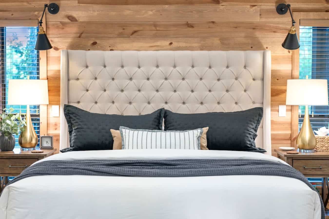 This bedroom is basically a five-star hotel moment with that perfectly tufted headboard, moody black bedding, those swing-arm reading lights, and windows that frame the treetops like living artwork.