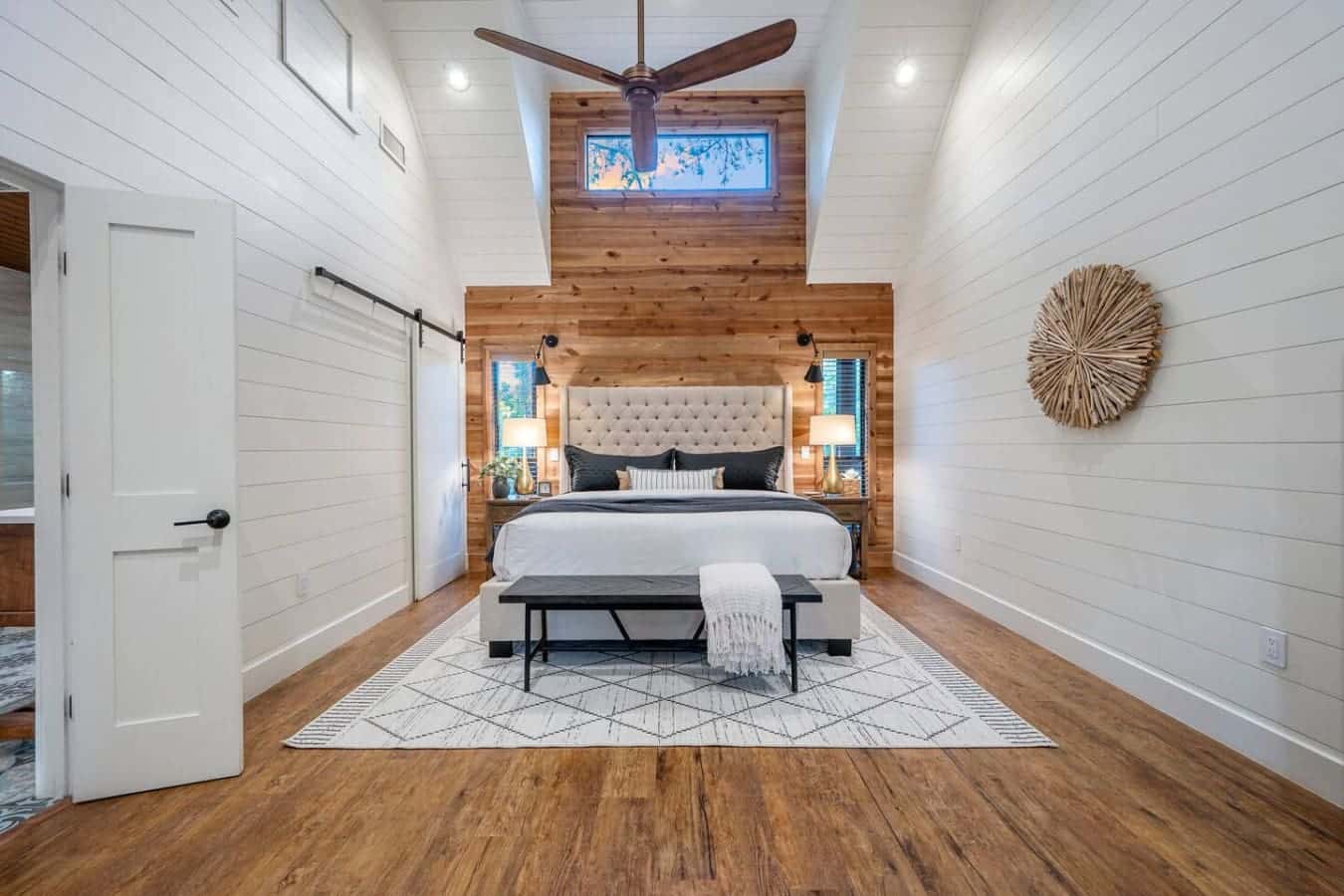 This primary bedroom hits different with those soaring ceilings, the wood accent wall framing the bed like it's a work of art, natural light pouring in from every angle, and a layout that somehow makes a king bed feel cozy instead of massive.