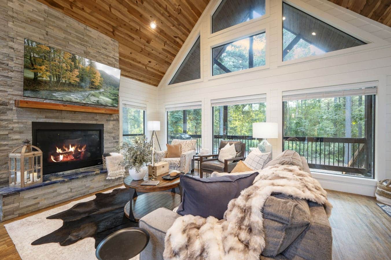 This living room basically has it all—a stone fireplace, wall-to-wall views of the trees, natural light pouring in from every angle, and enough cozy seating to gather everyone around without feeling cramped.