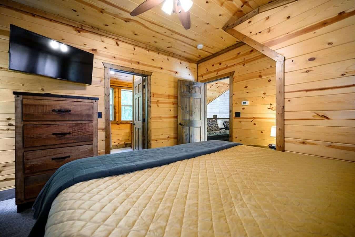 Experience the perfect blend of rustic charm and modern entertainment in this cabin bedroom, where a cozy bed meets the allure of a sleek television for a night of comfort and relaxation.