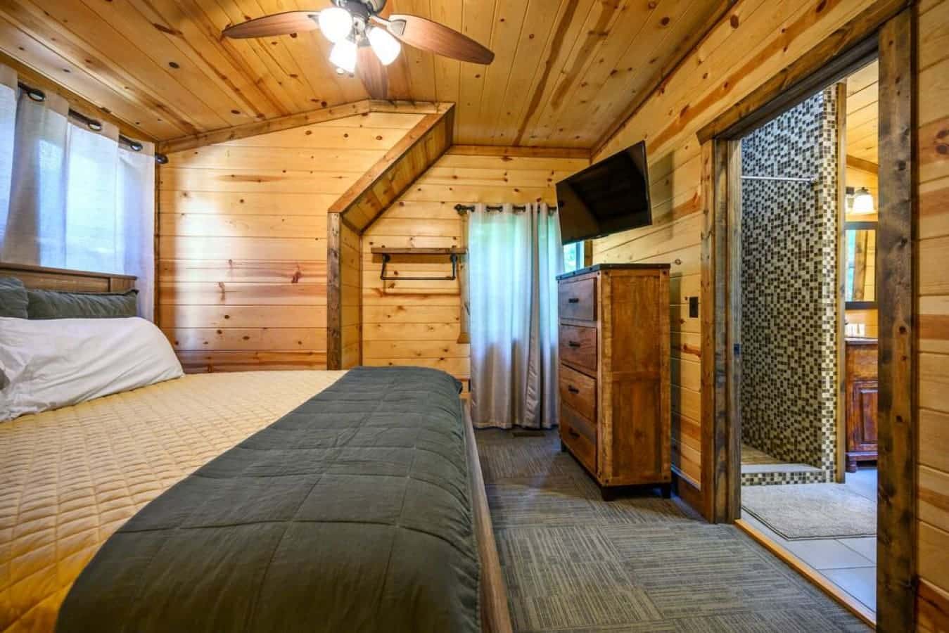 Savor a cozy night in this cabin bedroom, where the ambiance of a crackling fireplace is complemented by the modern entertainment of a wall-mounted television, offering the best of both worlds.