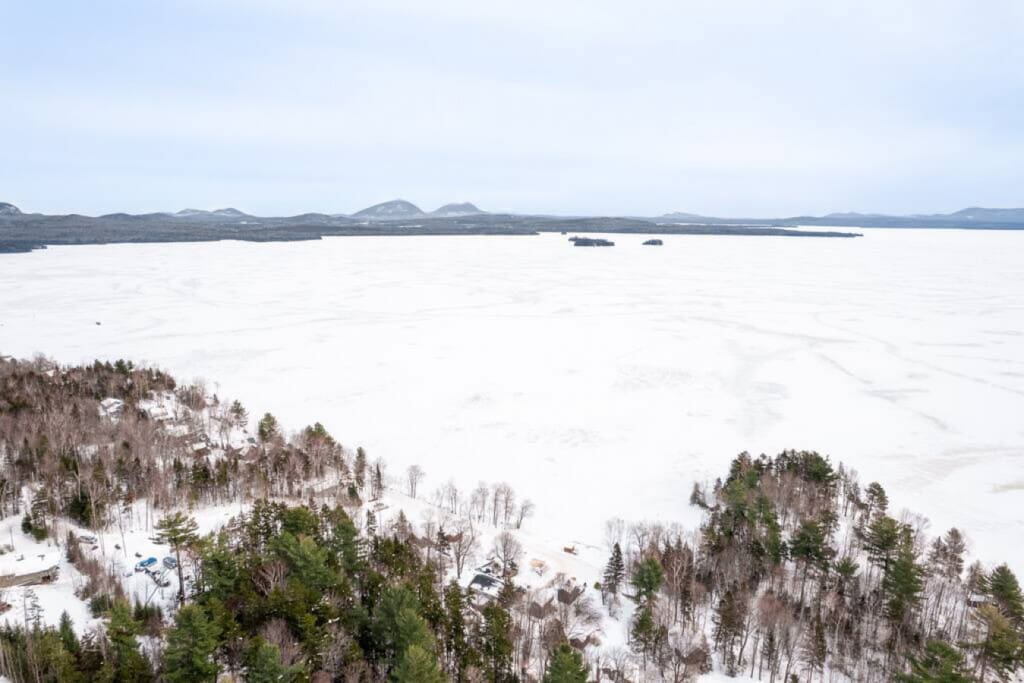 Imagine waking up to this—a pristine frozen lake stretching out in front of you with mountains in the distance and your own slice of Maine wilderness right outside your door.