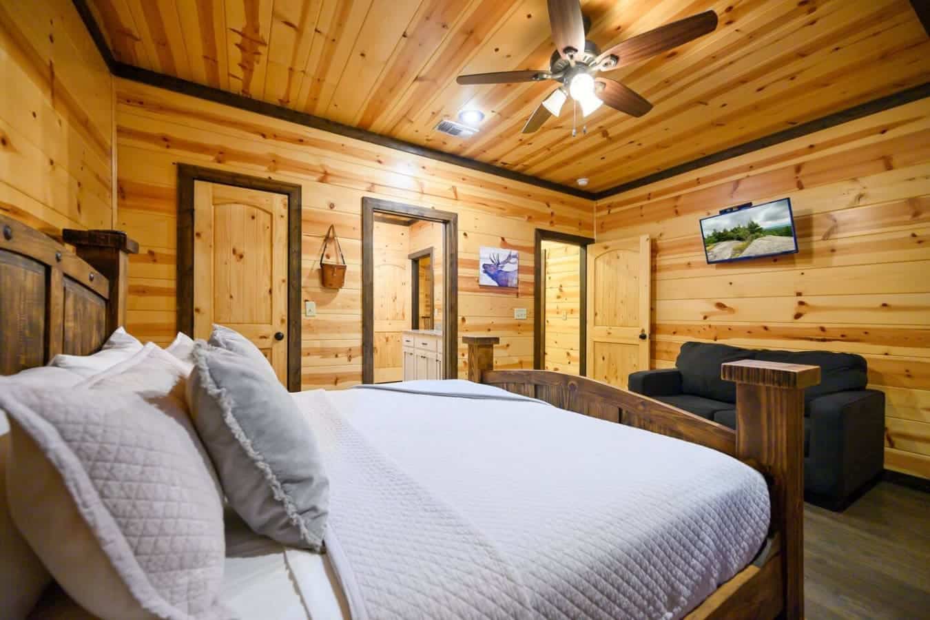 This master suite's got the whole package—a king bed with cloud-soft linens, your own cozy reading nook, dual closets, a ceiling fan, and windows that frame the forest, all wrapped up in that warm wood that makes you never want to leave.