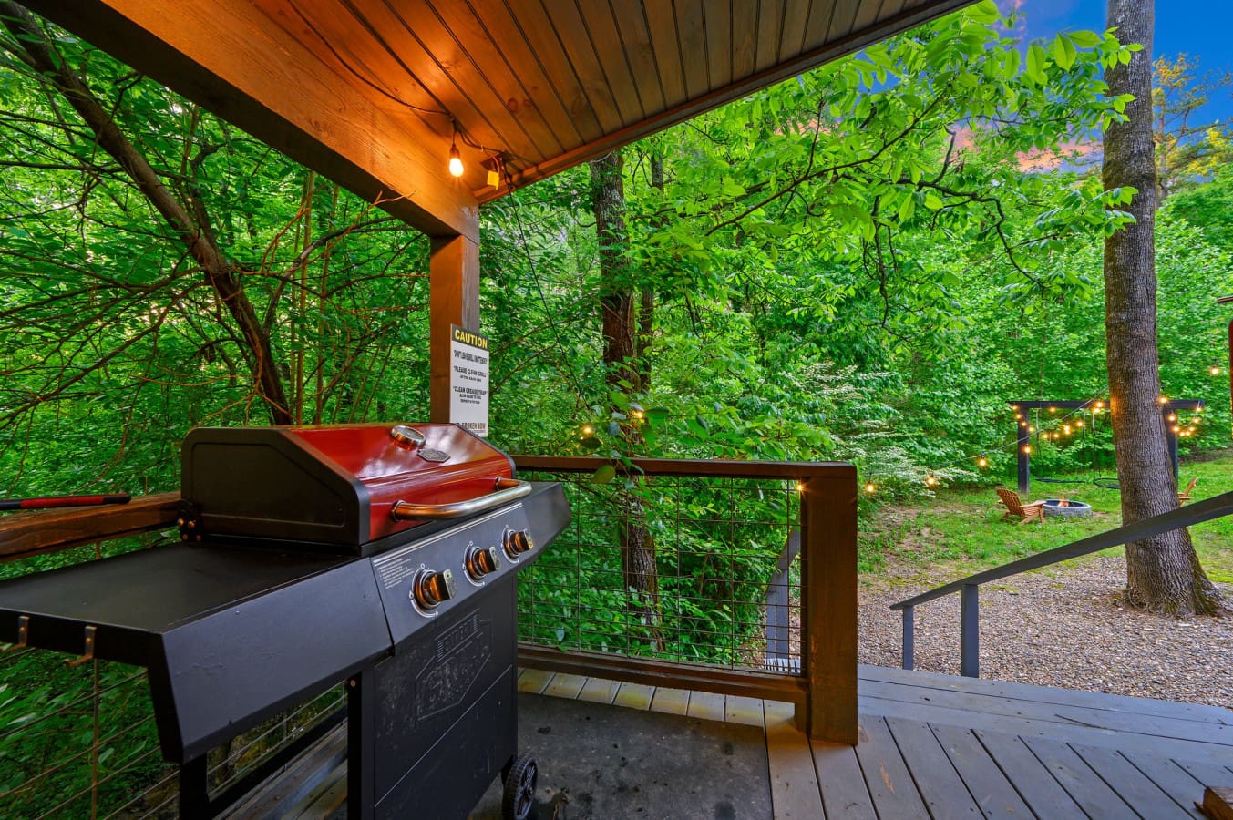 The deck is equipped with a gas grill for cooking and overlooks a rustic backyard with a fire pit area.