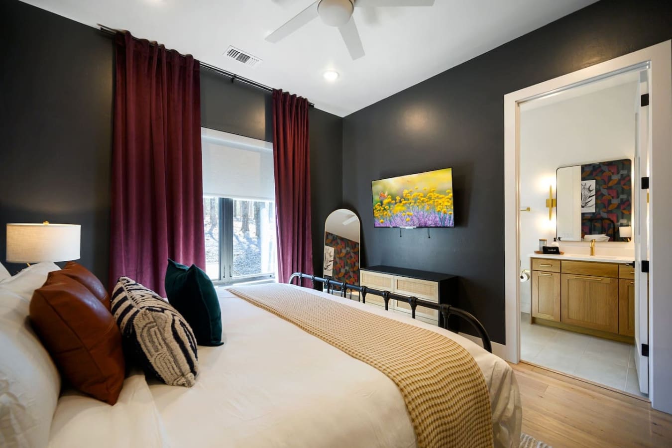 This master bedroom is basically the perfect blend of moody elegance and comfort, with those dramatic dark walls, rich burgundy curtains, a bright sunny window, and a spa-like ensuite that makes you feel like you're staying somewhere seriously fancy.