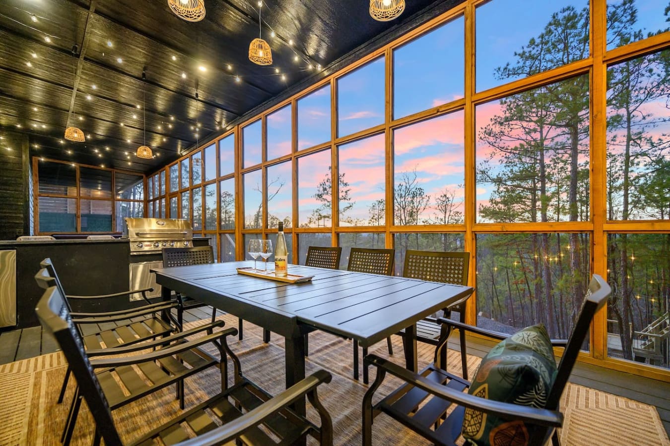 This screened-in dining space with floor-to-ceiling windows, twinkling overhead lights, and that jaw-dropping sunset view basically lets you feel like you're floating in the treetops while you eat dinner.