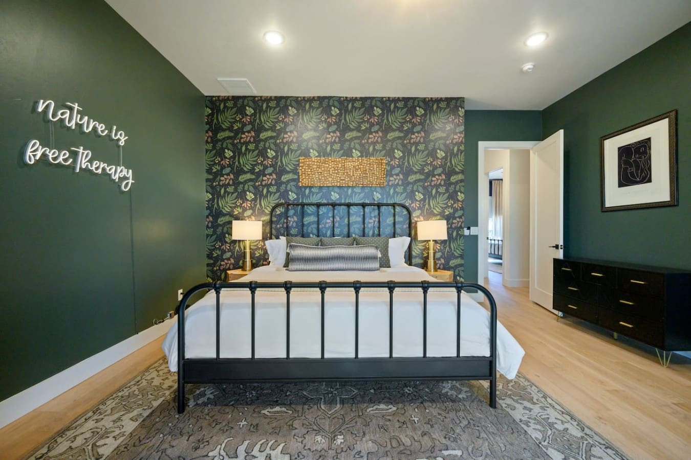 This primary bedroom is basically the perfect sanctuary with those rich forest-green walls, statement botanical wallpaper as a stunning headboard backdrop, moody black metal bed frame, and warm brass bedside lamps that all come together to make you never