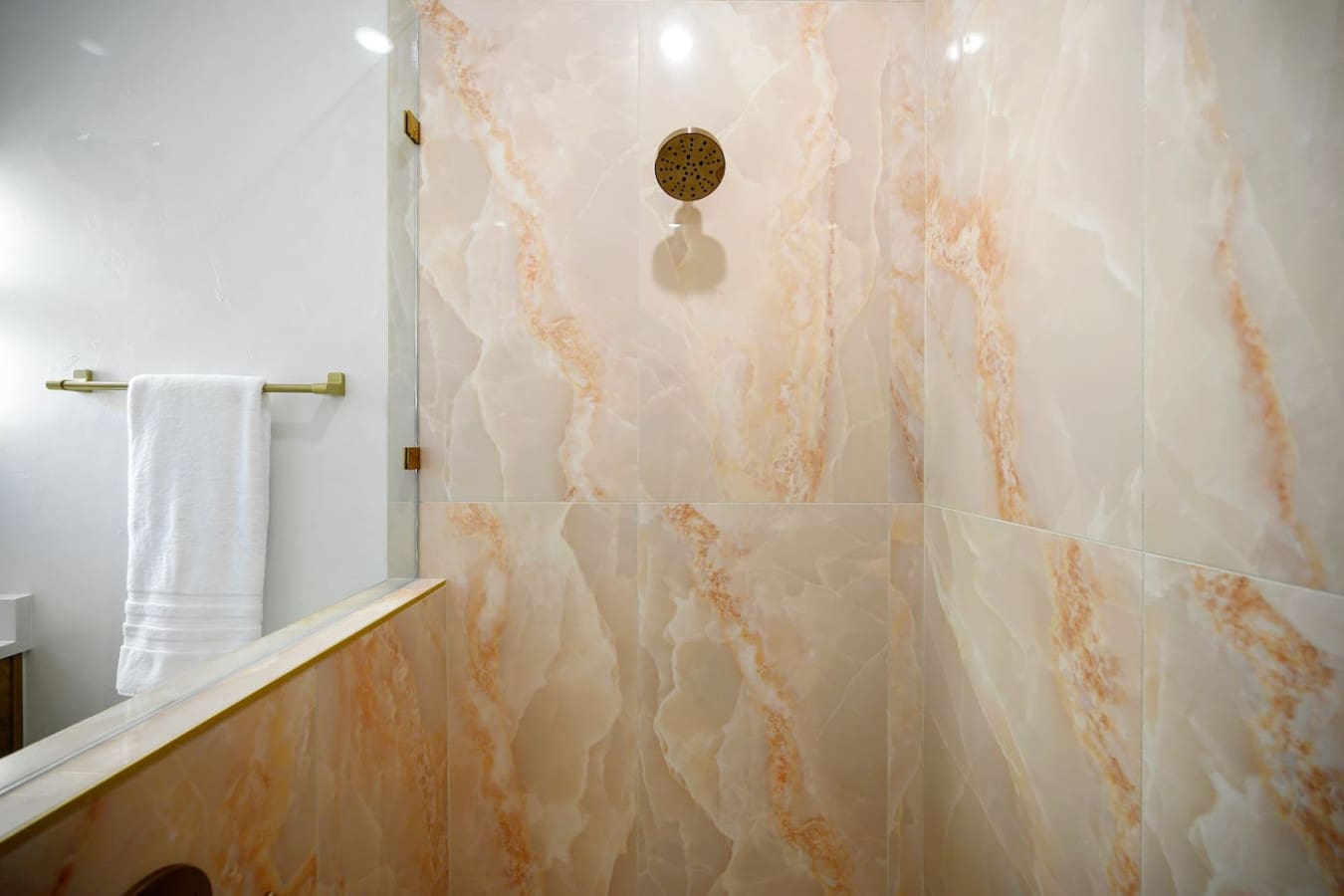 This marble-look shower with those gorgeous peachy veining details and brass rainfall showerhead is basically the kind of spot where you'll find yourself taking way longer showers than you probably should, just because it feels that good.