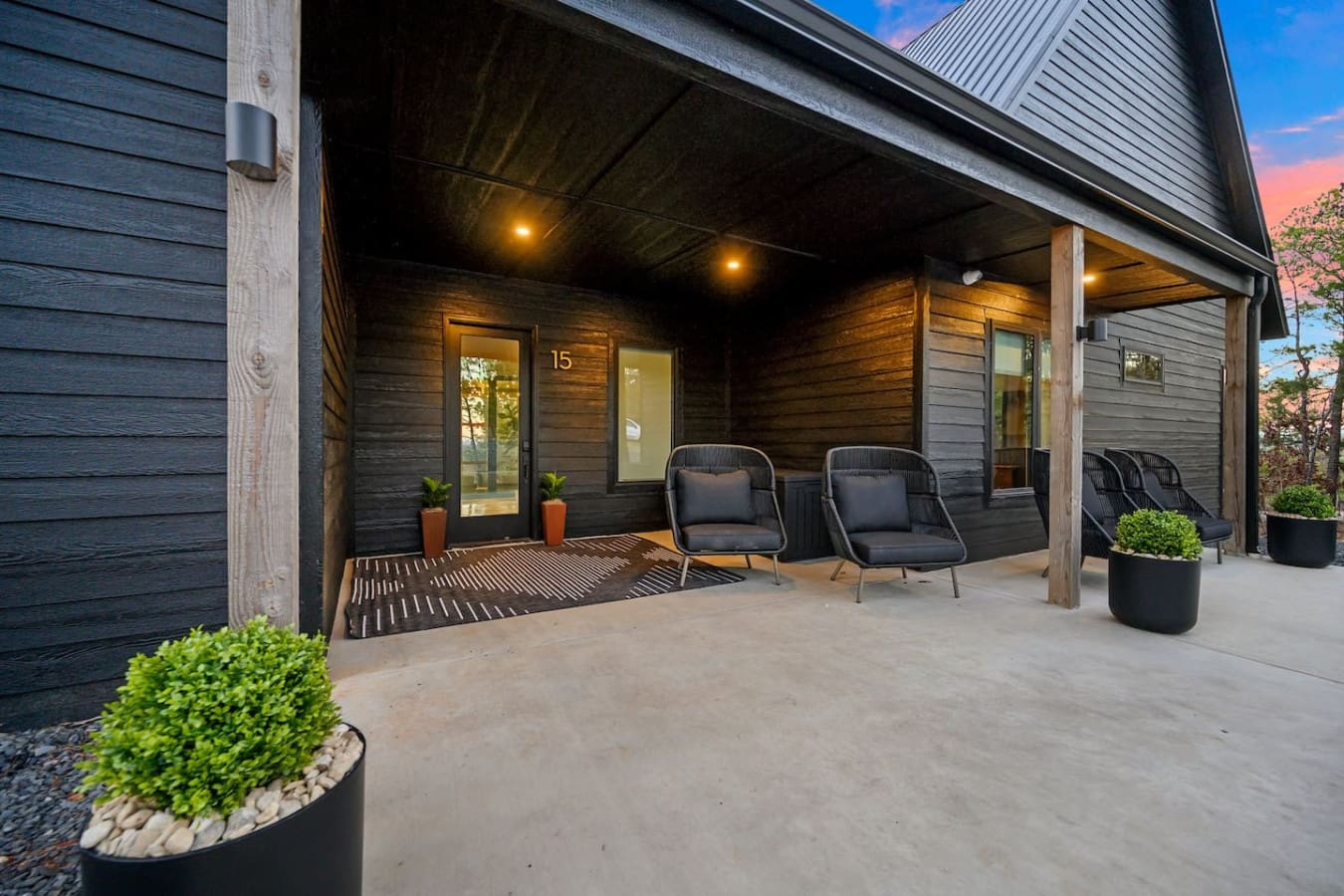 This covered patio with its moody wood siding, warm overhead lighting, and those sleek modern chairs basically gives you the perfect setup to settle in with a book or just watch the sunset without worrying about the weather.