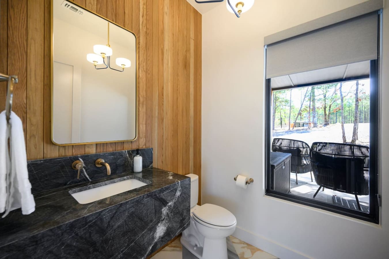 This bathroom is basically the perfect blend of spa luxury and natural views—sleek dark marble vanity, brass fixtures, and a huge window framing those peaceful forest and deck vibes so you can soak in the scenery while getting ready.