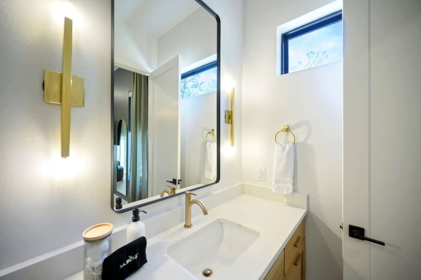 This bright, airy bathroom with its sleek black-framed mirror, warm brass fixtures, and those high windows flooding in natural light basically makes getting ready feel like a spa moment every single day.
