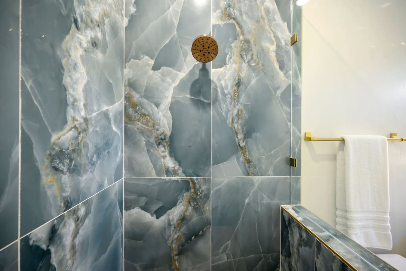The dramatic marble-look tile work in this shower, with those gorgeous veining details and brass fixtures, basically makes you feel like you're stepping into a luxury spa every time you want to rinse off.