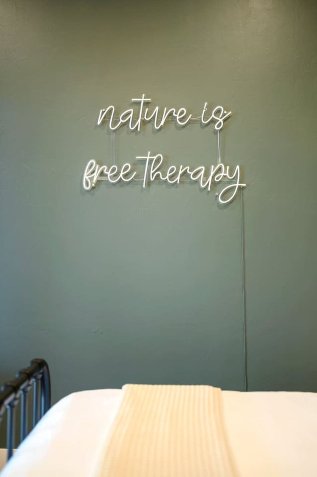 This bedroom is basically the perfect calm escape with those soothing sage walls, neon sign reminder that nature is free therapy, and that cozy reading nook by the window—it's like the space itself is telling you to slow down and just breathe.