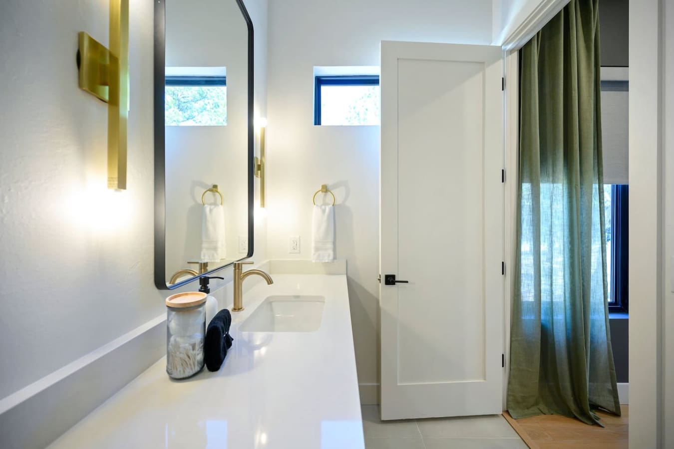 This sleek double vanity with its matching brass faucets, soft warm lighting, and those high windows letting in natural light is basically the kind of bathroom where you'll actually want to linger over your morning routine.