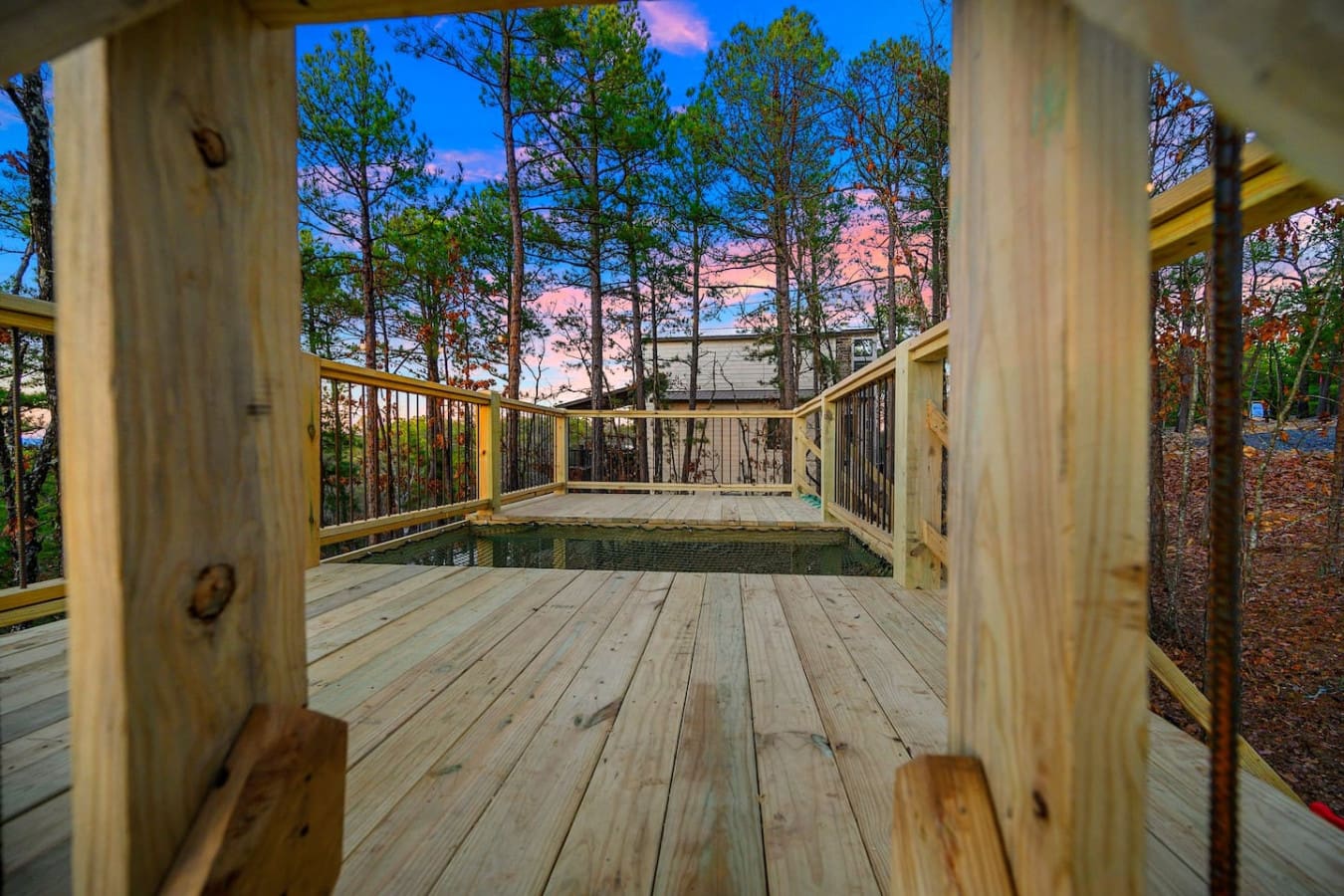 You're basically standing on your own private forest-floating deck with that jaw-dropping sunset painting the sky pink and gold, while the tall pines frame everything like nature's own gallery walls.