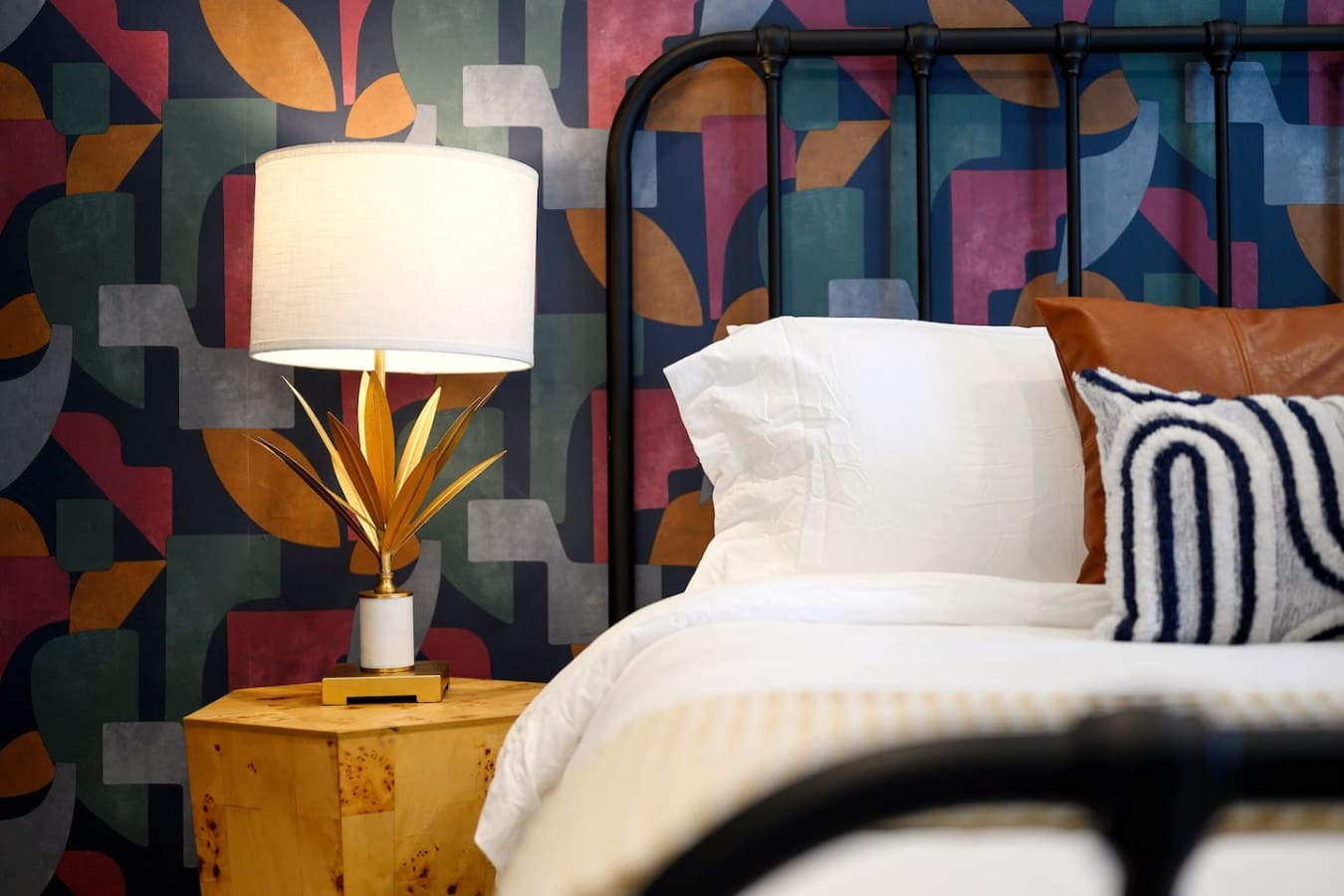 This bedroom totally captures that modern eclectic vibe with the bold geometric wallpaper, brass-accented lamp, crisp white bedding, and that black metal bed frame that somehow feels both artistic and super inviting.